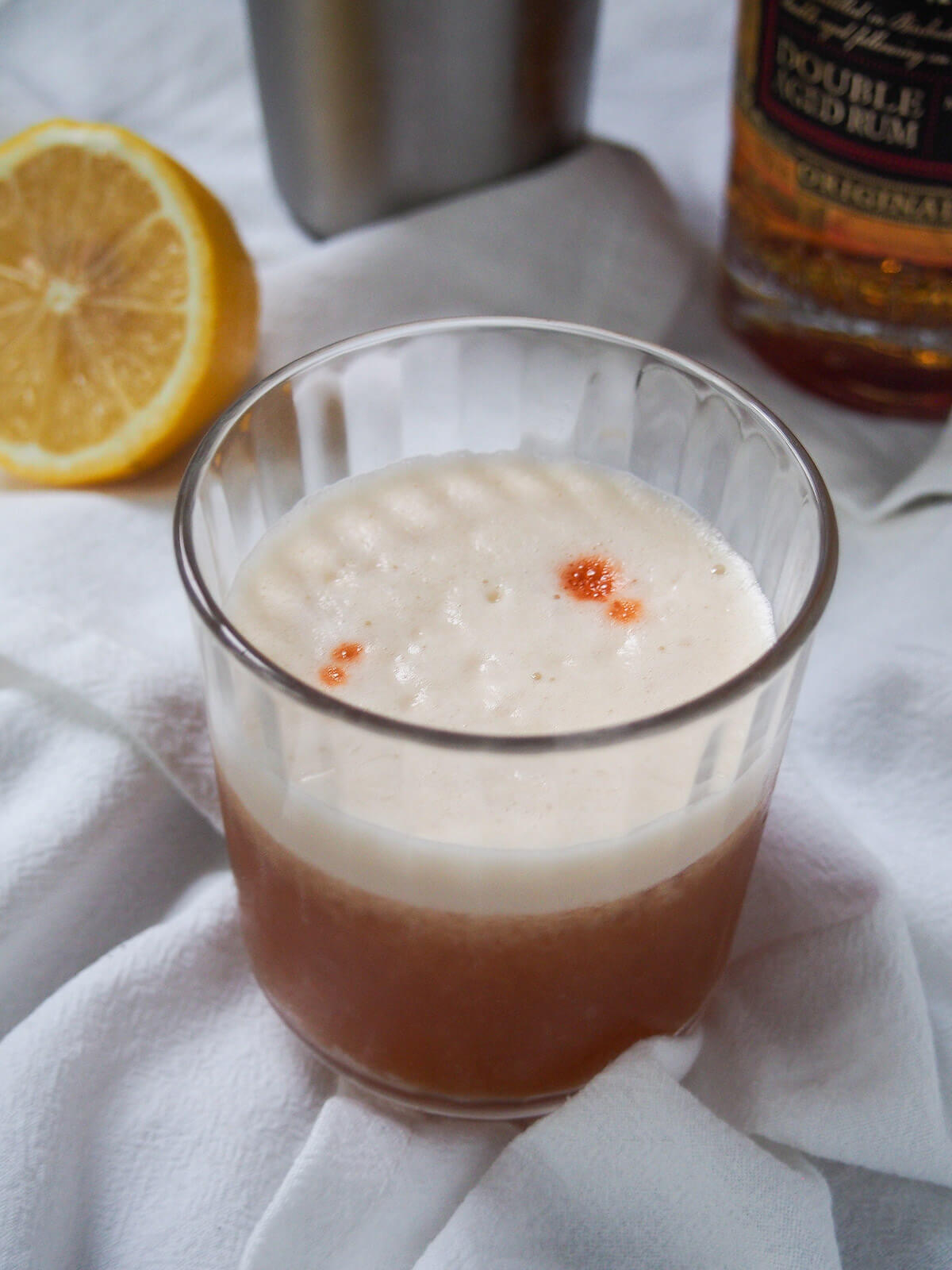 glass of rum sour with part of bottle and lemon in background.