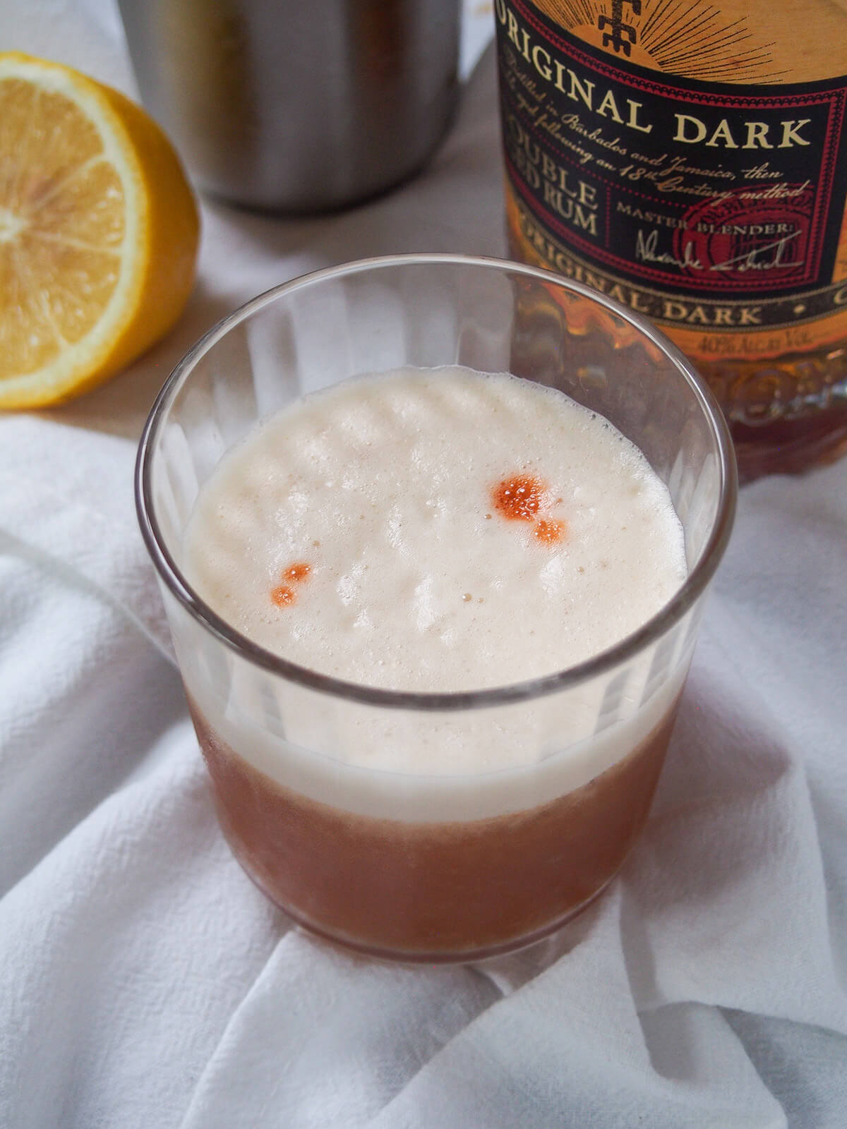 glass of rum sour with bottle of dark rum behind.