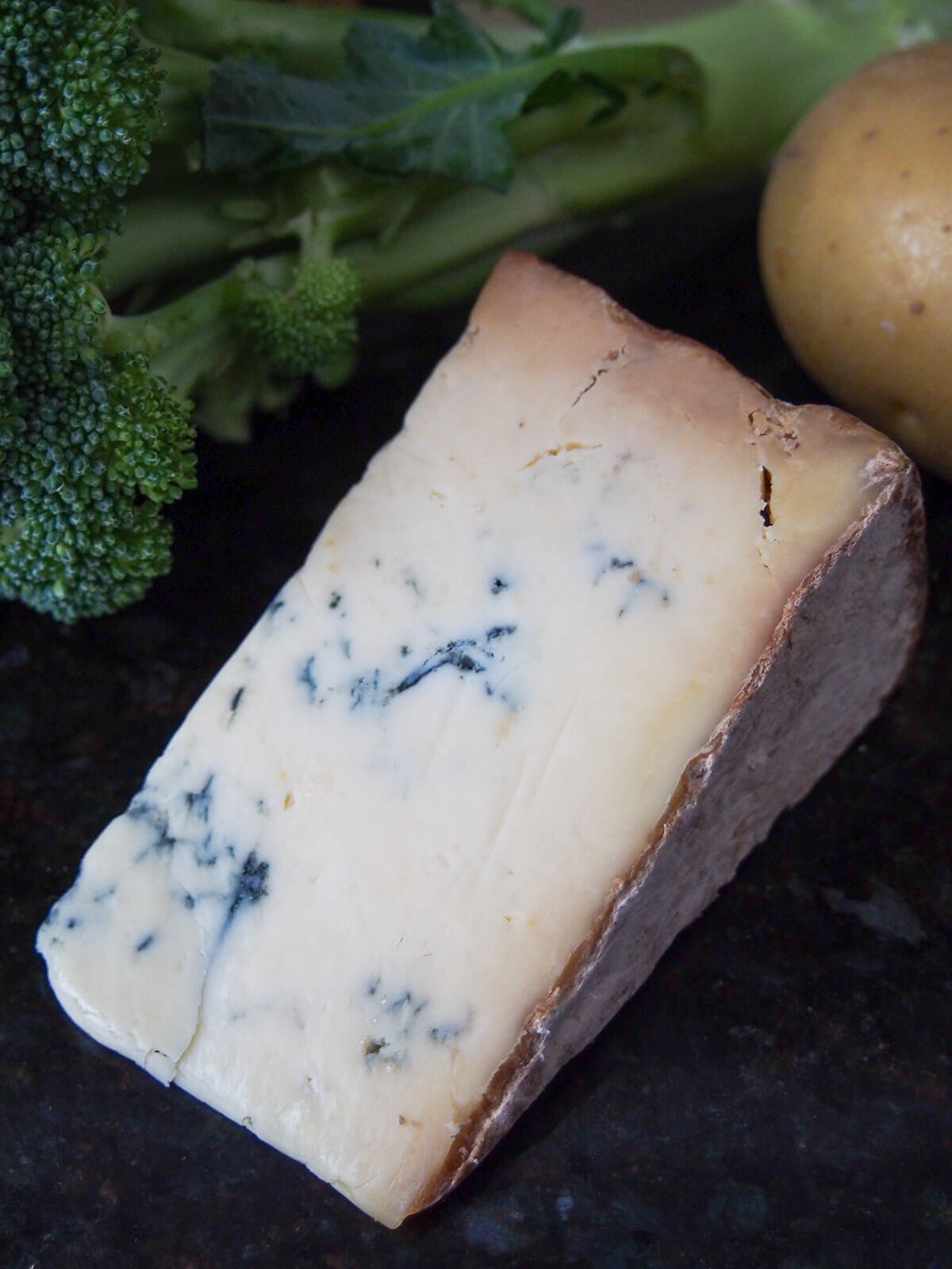 block of Stilton cheese with broccoli and potato in background behind.