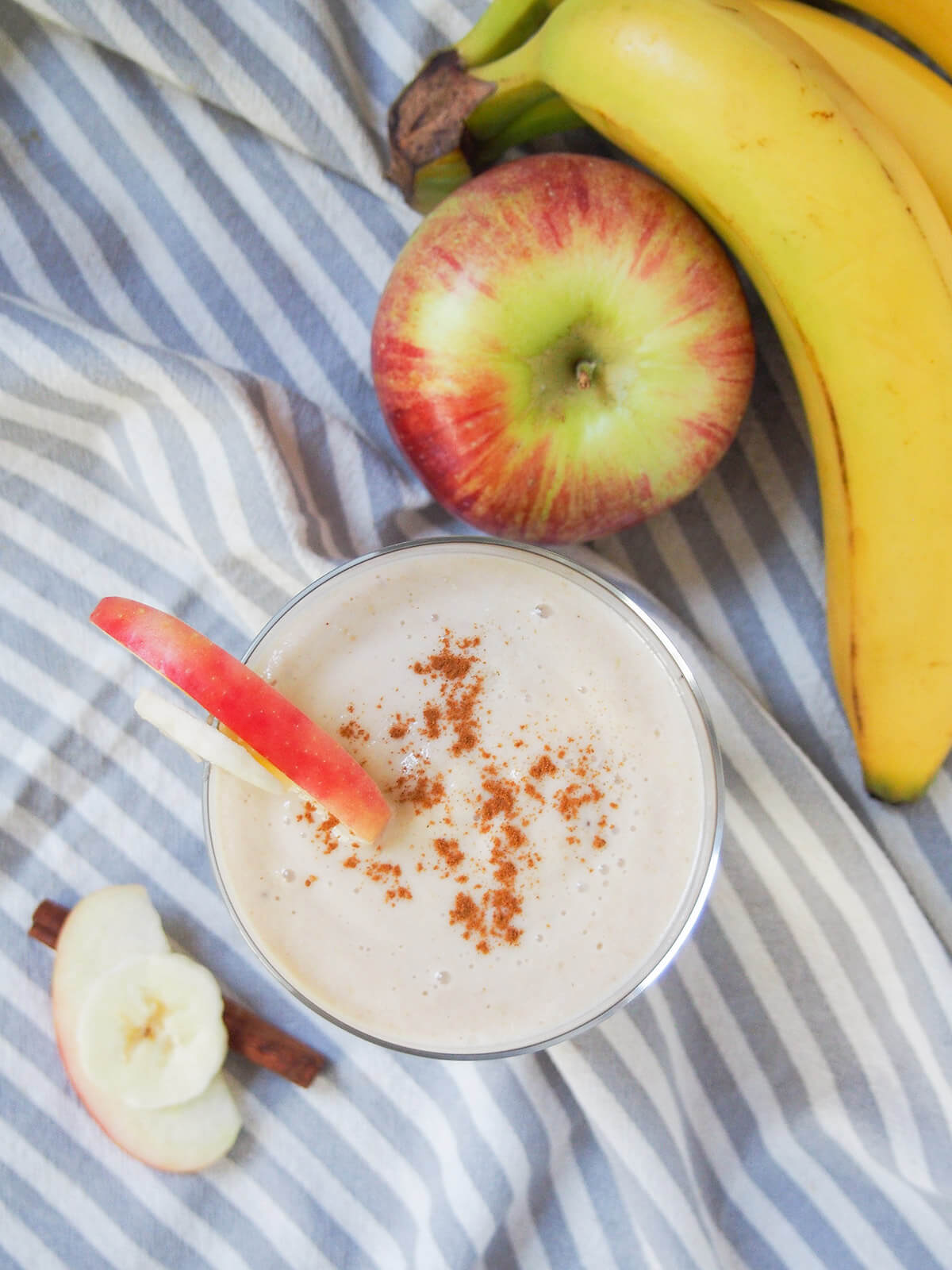 Trying to be healthier doesn't have to mean lots of work or tasteless options. This apple banana smoothie is thick, fruity, and really easy to make using common ingredients. It's almost like drinking apple pie! glass of apple banana smoothie from overhead with apple and bunch of bananas above glass.