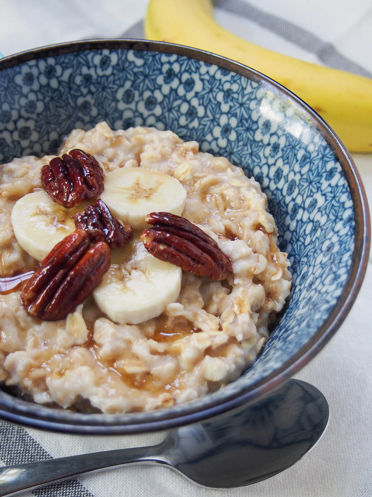 part view of bowl of banana oatmeal with banana in background behind and spon below