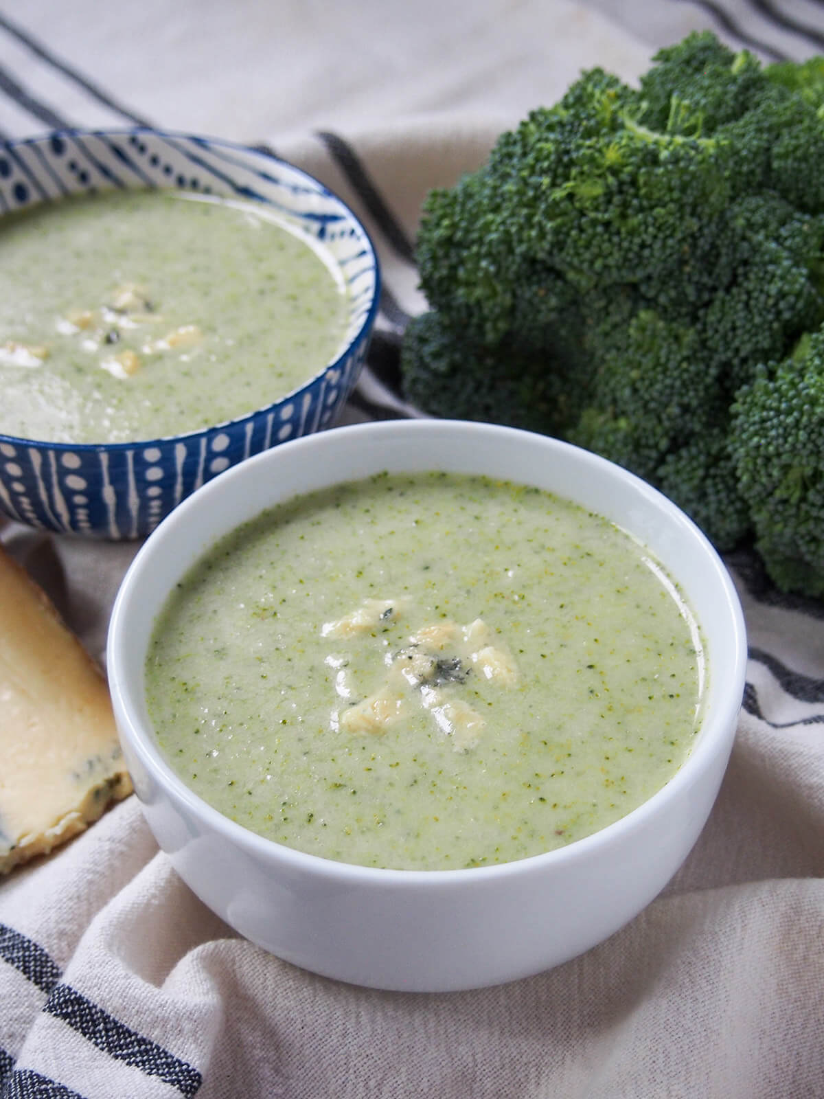 white bowl filled with broccoli and stilton soup with broccoli head and other bowl behind.