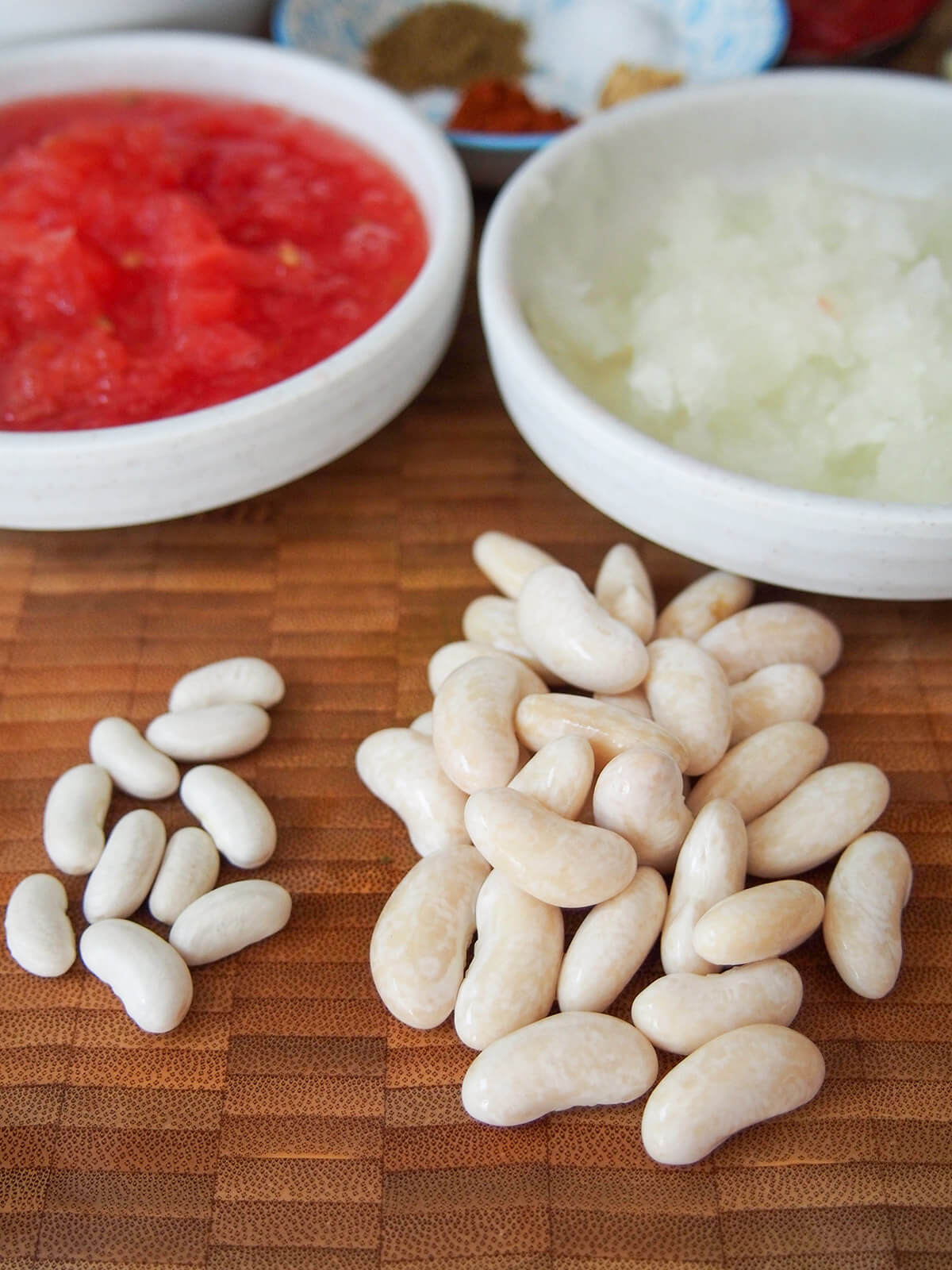 dry cannellini beans to left next to soaked beans on right with prepared vegetables in dishes behind.
