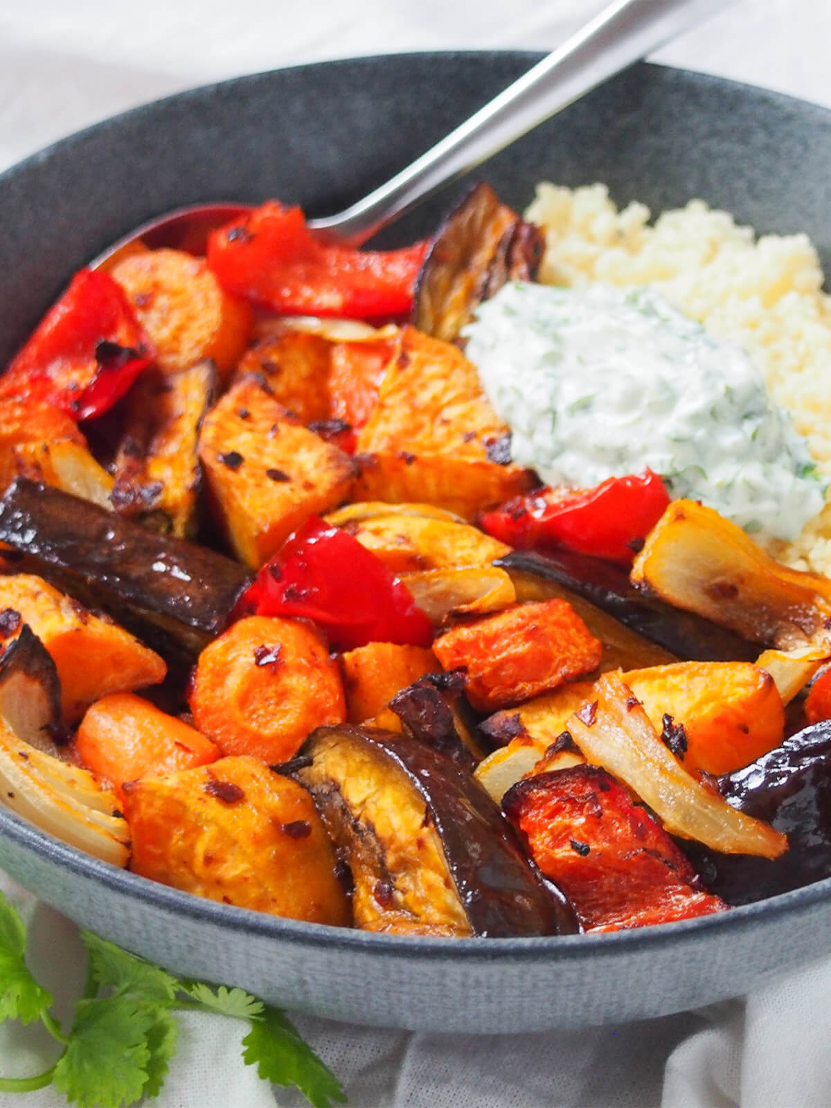 bowl of harissa roasted vegetables from side with spoon at back on bowl.