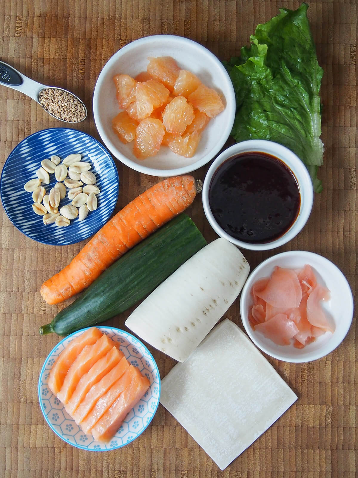 bowls with sashimi salmon, pickled ginger, plum sauce and grapefruit with cucumber, carrot and daikon in middle.