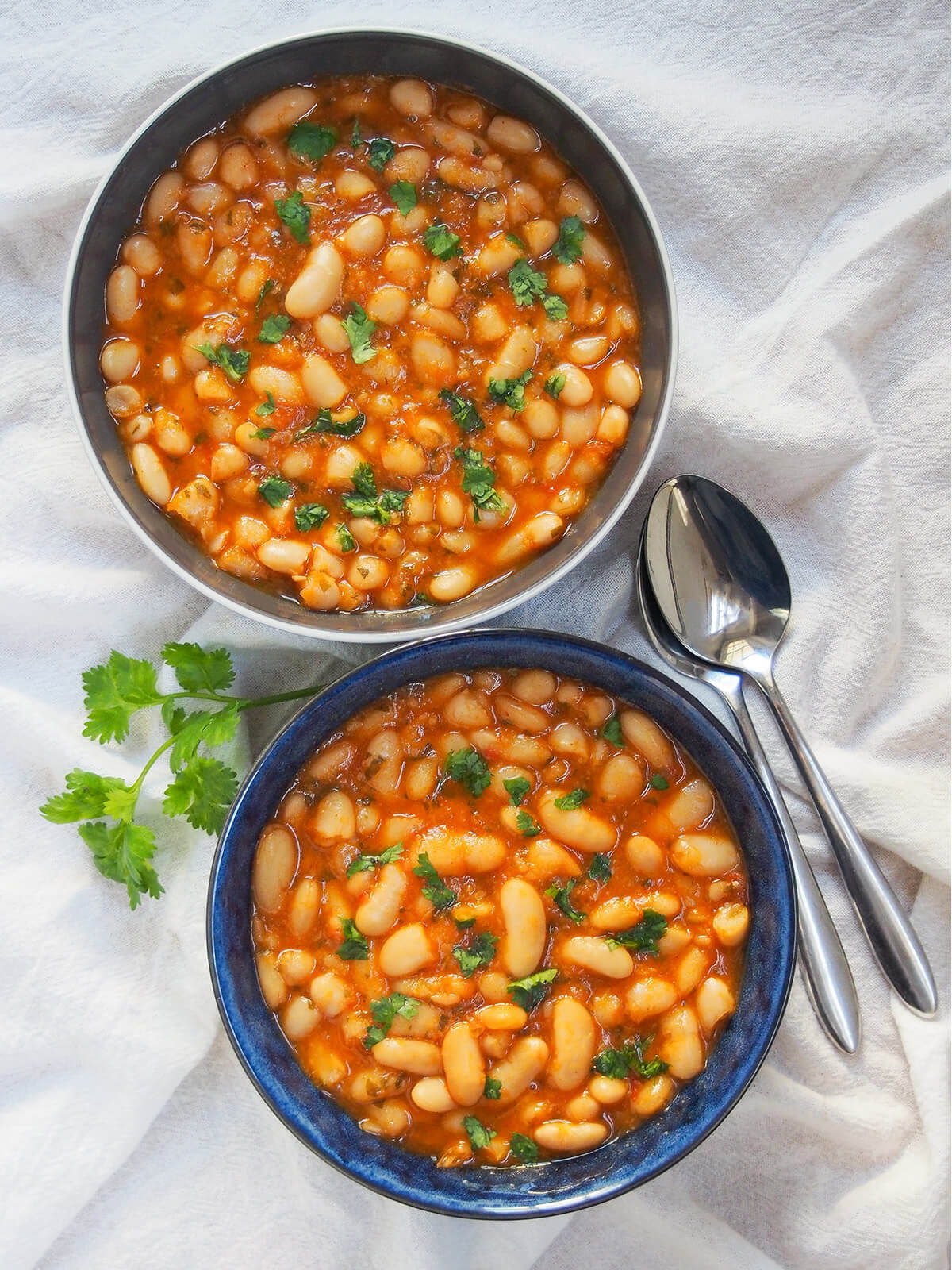 two bowls of loubia Moroccan white bean stew with spoons to right.