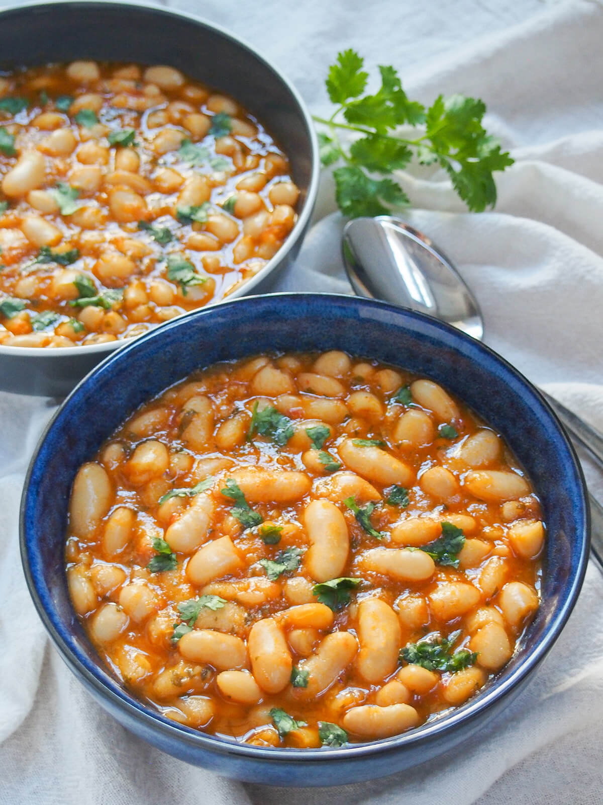 bowl of loubia Moroccan white bean stew in blue bowl with other bowls and spoons behind.
