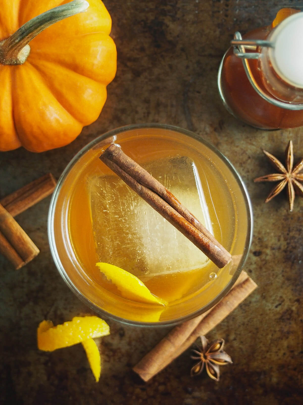 glass of pumpkin spice old fashioned from overhead with pumpkin above and spices around