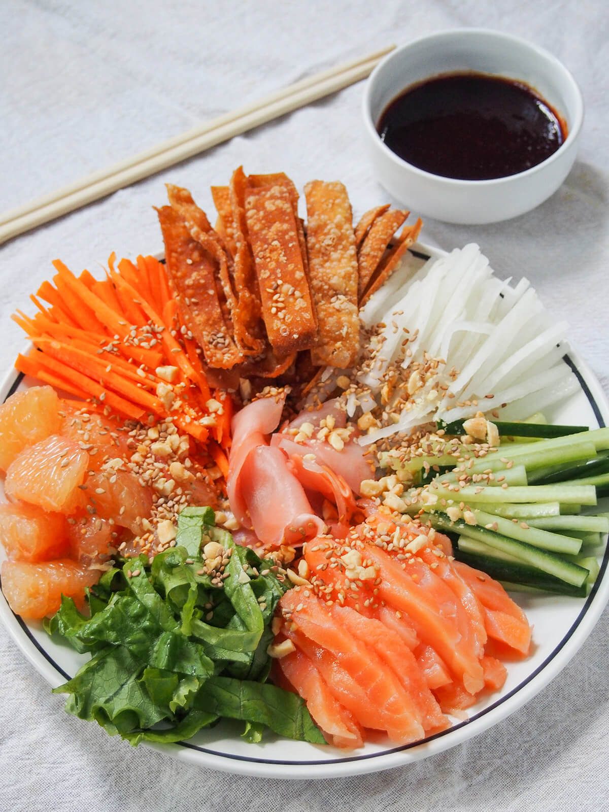 plate of yee sang prosperity toss with bowl of sauce as dressing behind.