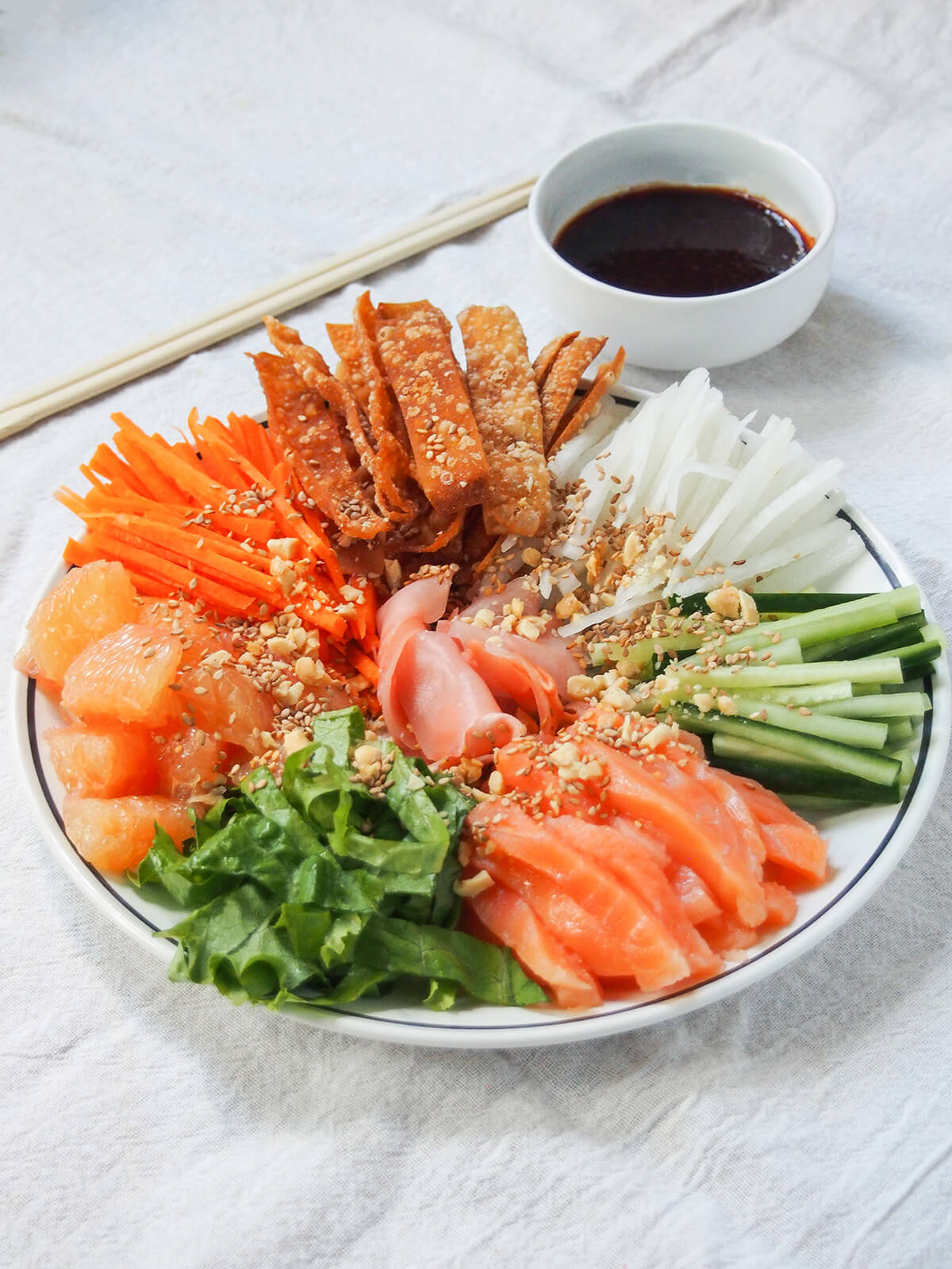 plate of yee sang prosperity toss with chopsticks and bowl of sauce behind.