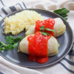 plate with two golabki, Polish stuffed cabbage rolls, with mashed potato behind and parsley garnishes.