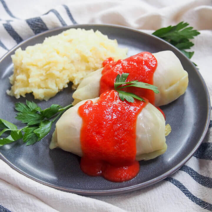 plate with two golabki, Polish stuffed cabbage rolls, with mashed potato behind and parsley garnishes.