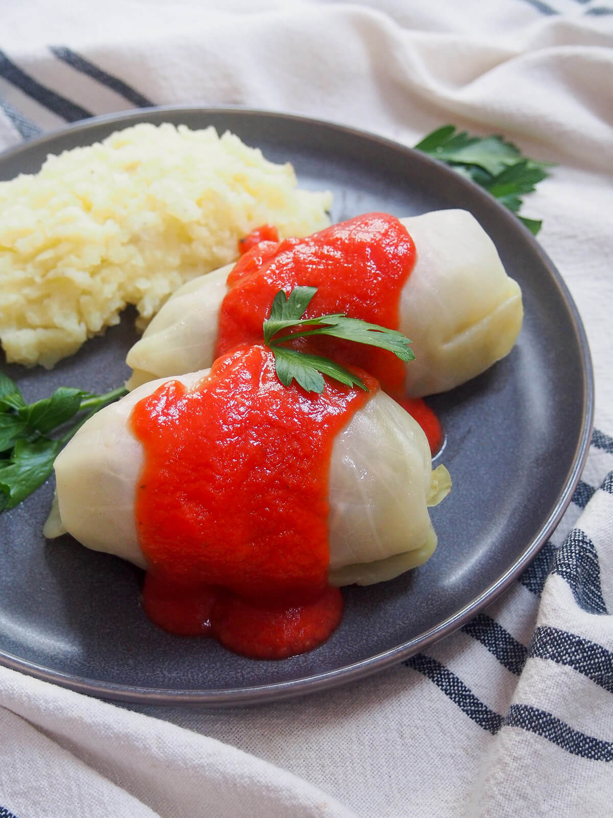two whole goabki, Polish stuffed cabbage rolls, on plate with mashed potato to side.