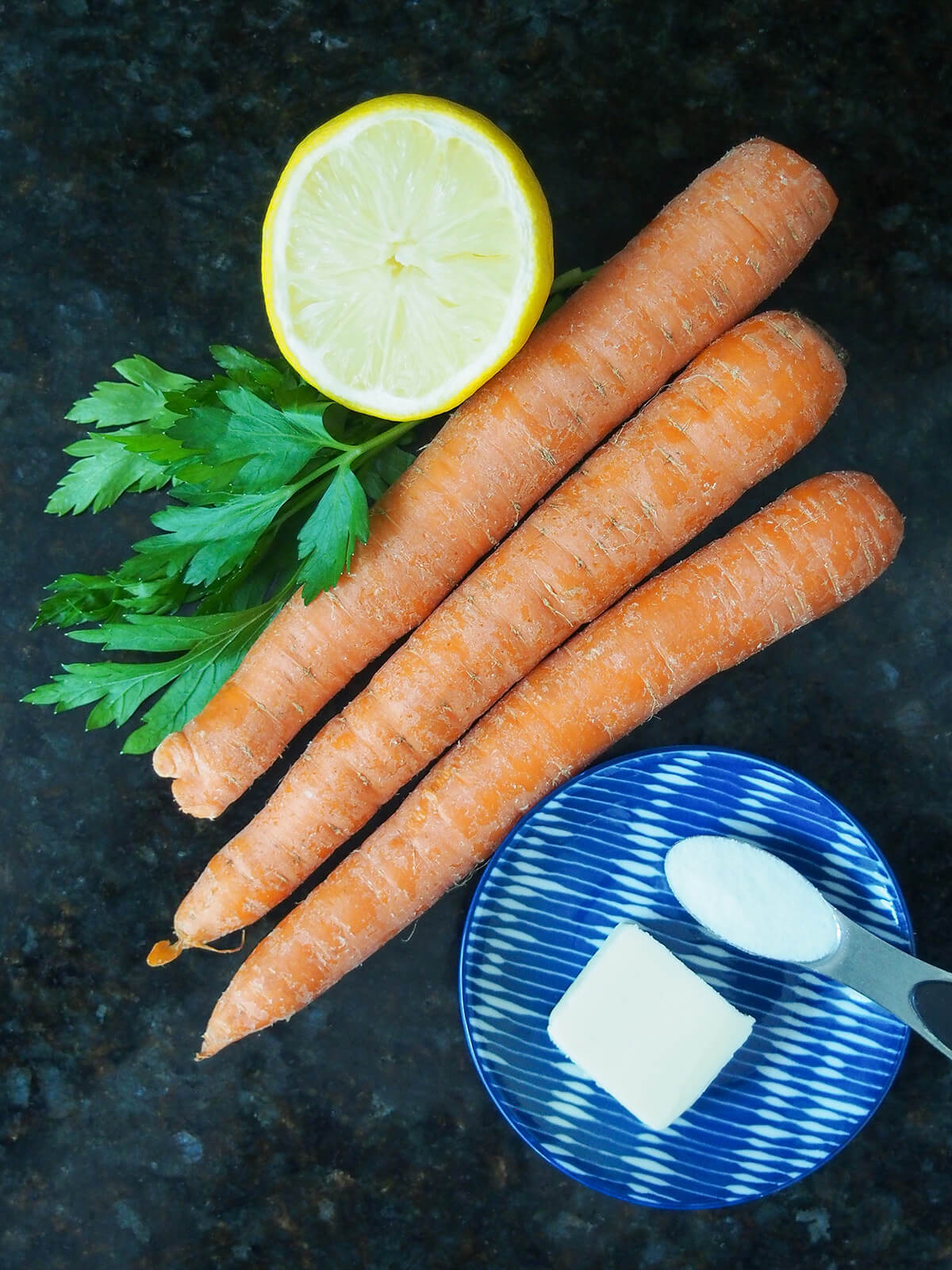 carrots, lemon, small bunch of parsley and dish with butter and sugar.