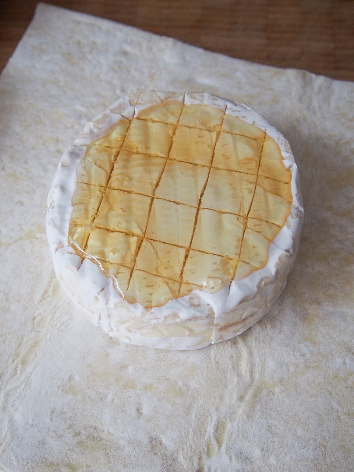 scored brie with honey on top sitting on piece of pastry.