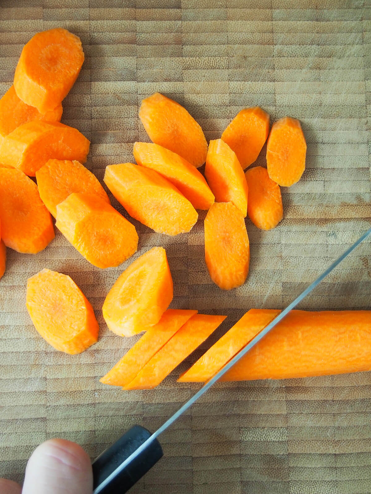 cutting a carrot on the diagonal on wooden board.