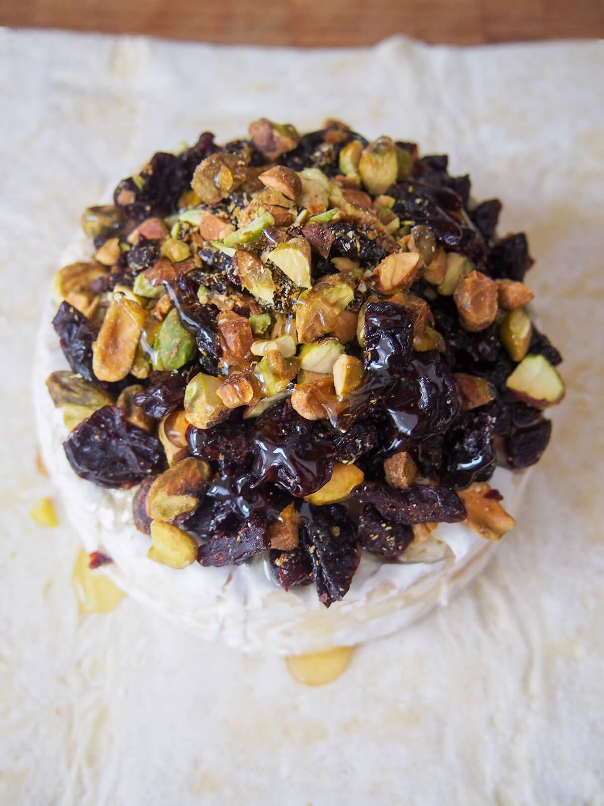 nuts and dried cherries stacked on top of brie round on pastry with honey drizzled on.
