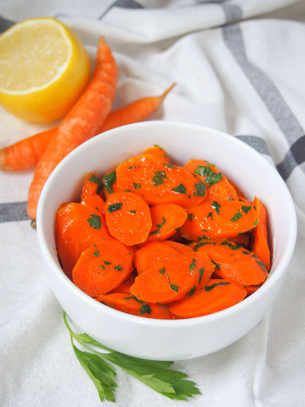 bowl of vichy carrots with small carrots in background and parsley to side.