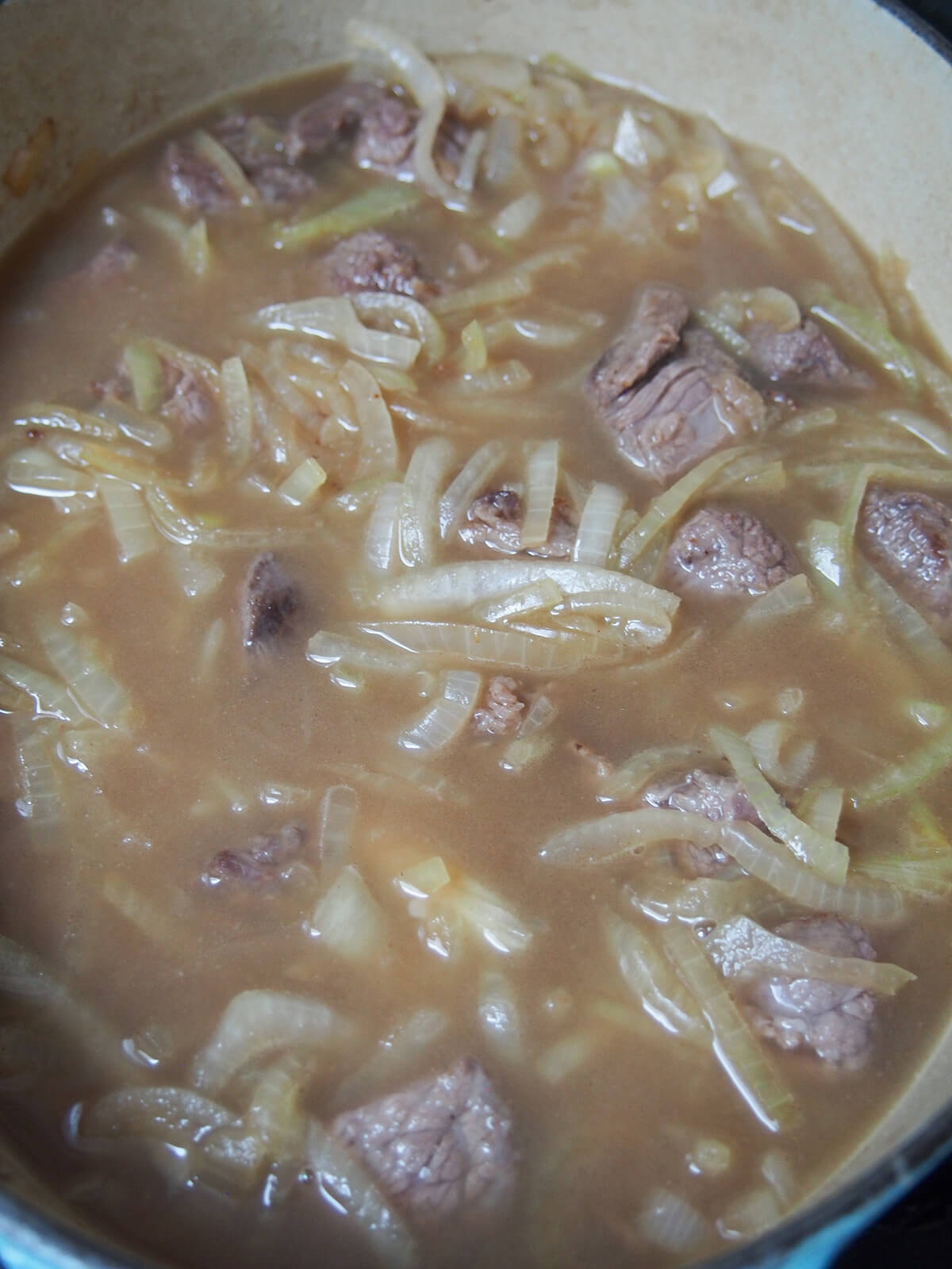 pot with beef, onions and stock with the onions and meat just showing above the liquid.