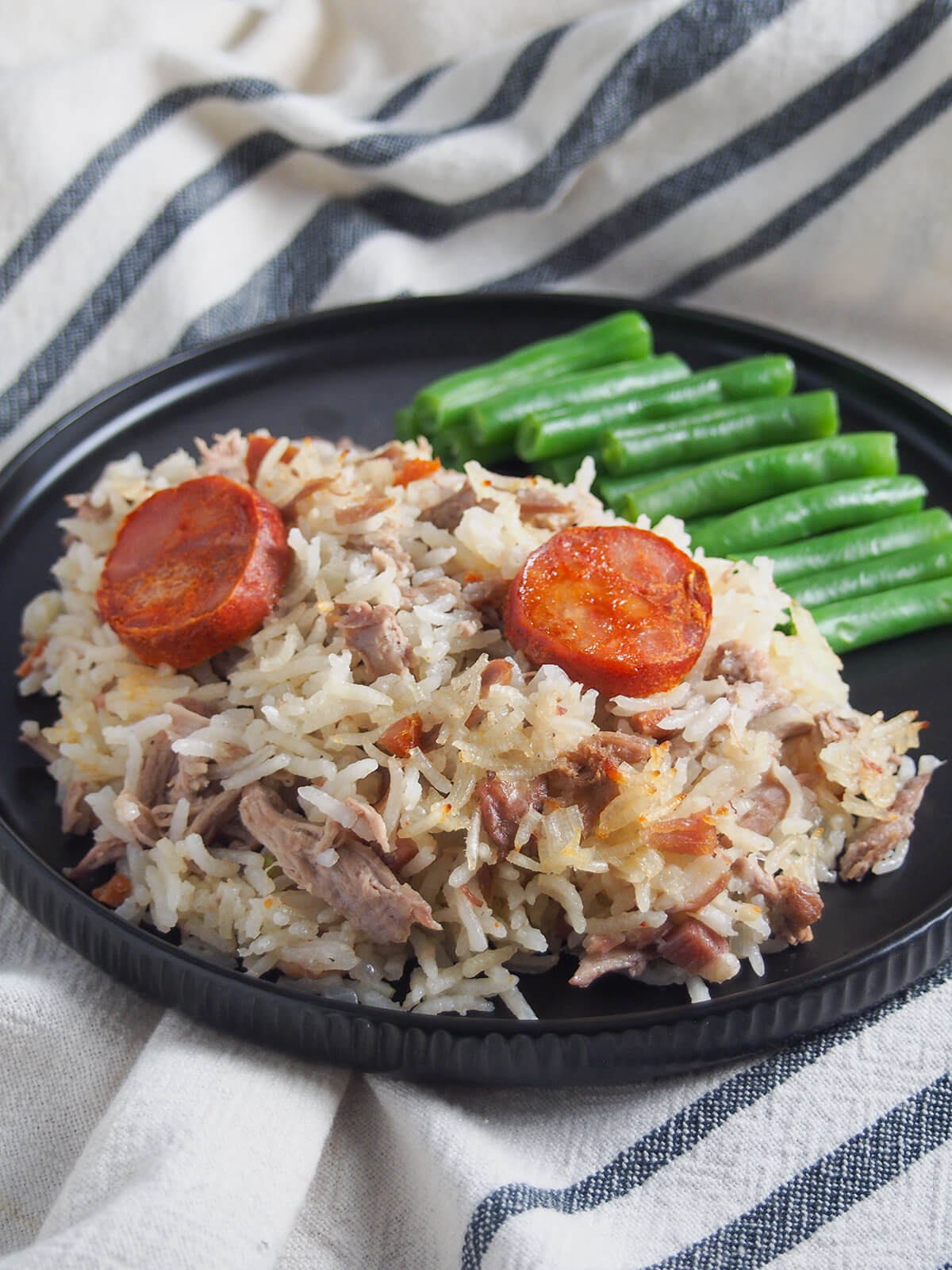 plate of arroz de pato Portuguese duck rice with green beans behind rice.