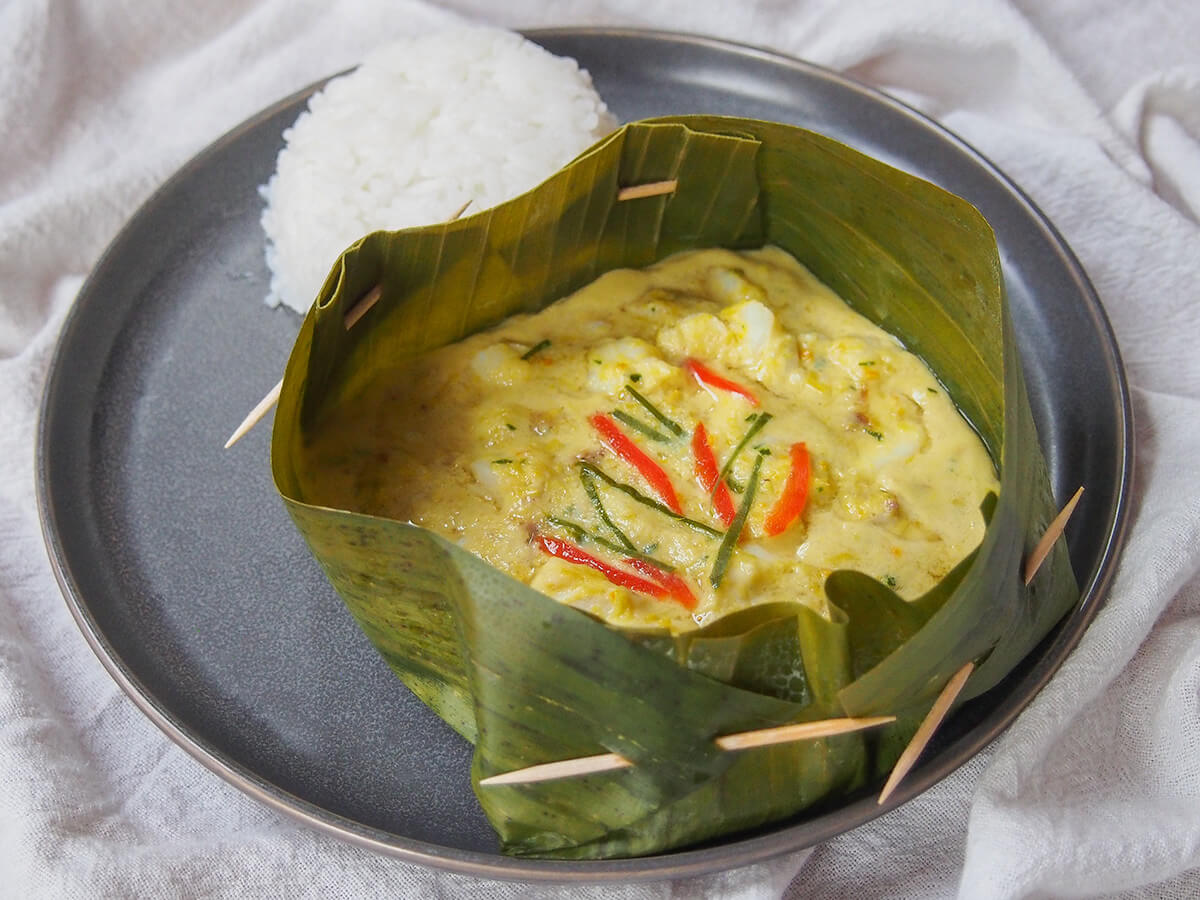 banana leaf boat filled with fish amok (amok trey) with rice behind.