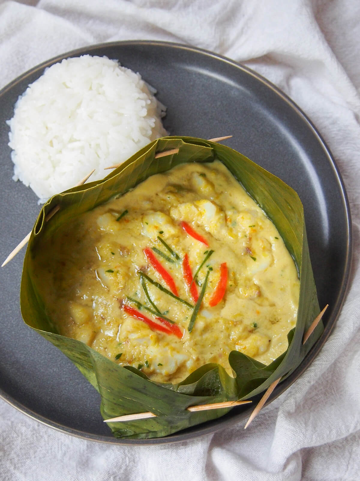 fish amok (amok trey) in banana leaf on plate from above with rice above.