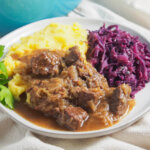 plate of hachee Dutch beef stew served with potato and red cabbage.