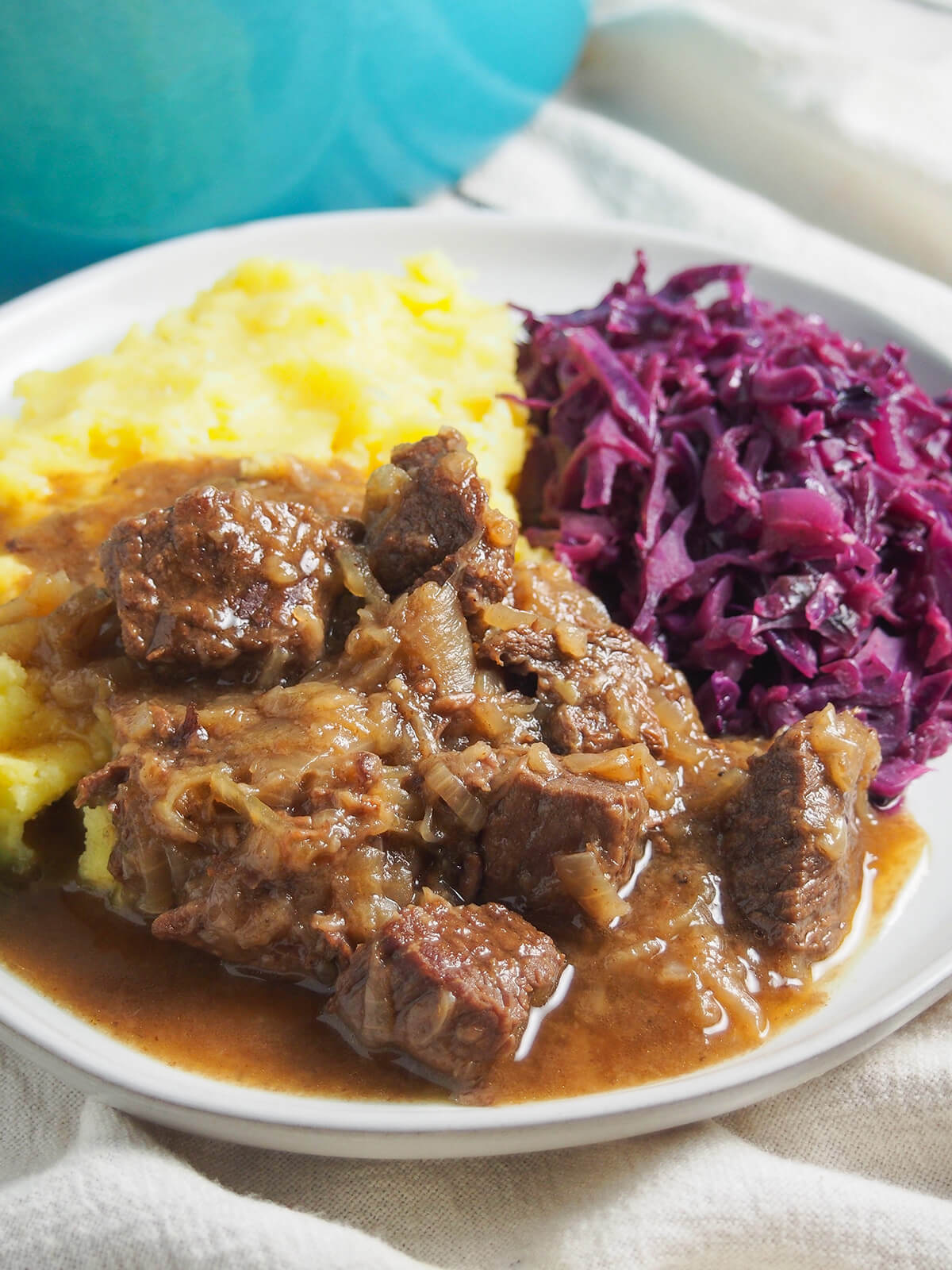close view of hachee Dutch beef stew with red cabbage and mashed potato behind.