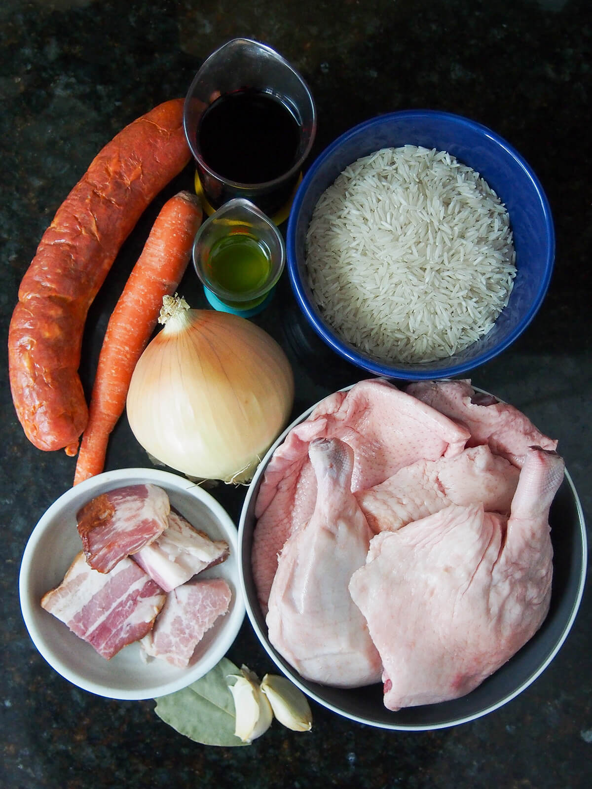 bowls with duck pieces, bacon, rice with onion, chorico, garlic, bay, carrot and wine to side.