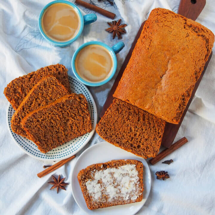 overhead view of loaf of ontbijtkoek Dutch spice cake with slices on plate and small plate with a slice with butter, vups of coffee between.