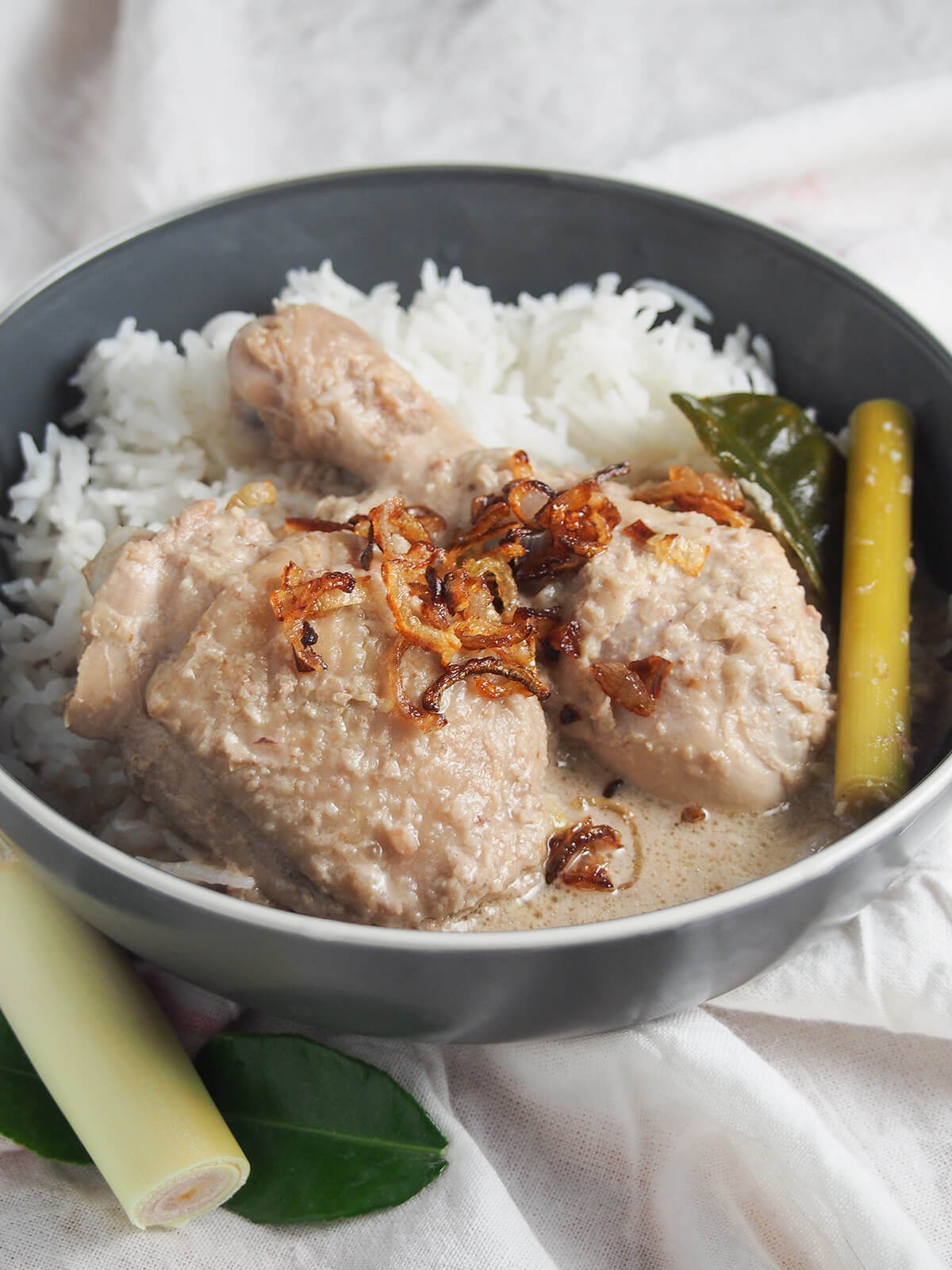 side view of bowl of opor ayam Indonesian coconut chicken served with rice.