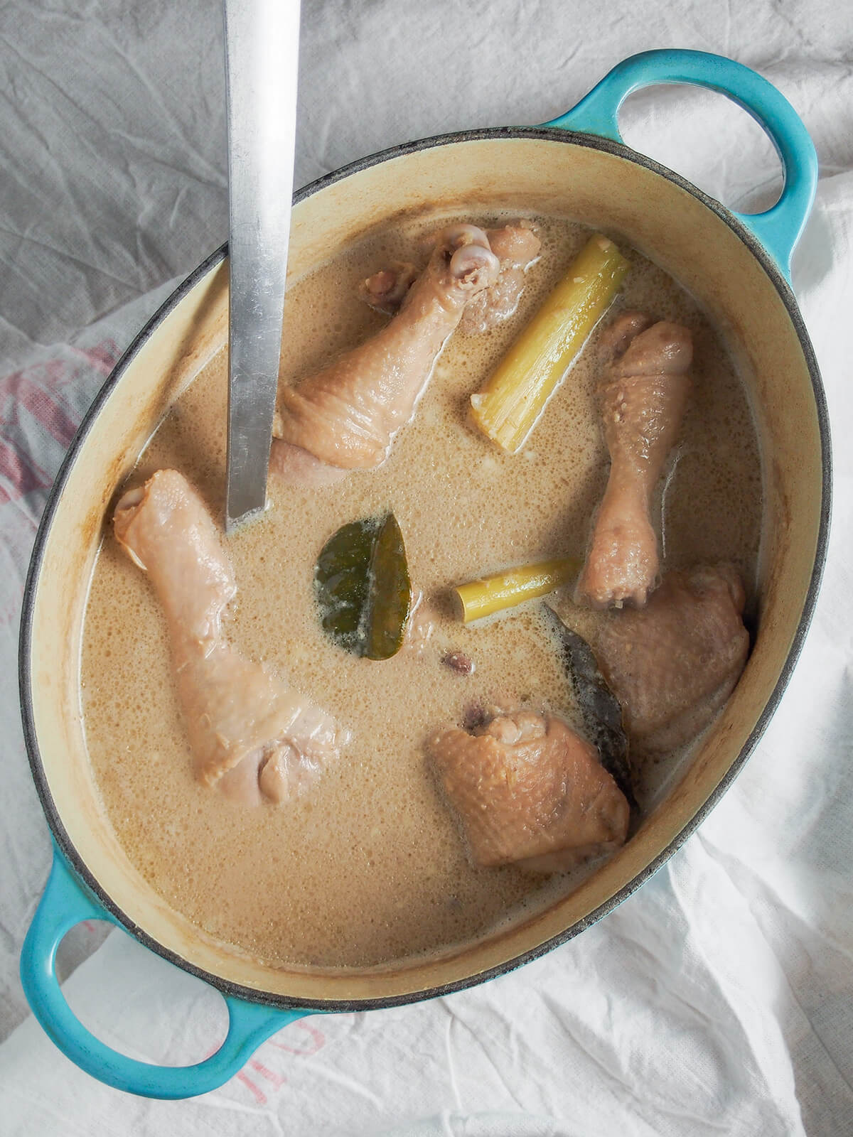 pot of opor ayam Indonesian coconut chicken with lemongrass stems, lime leaves and chicken showing through sauce.