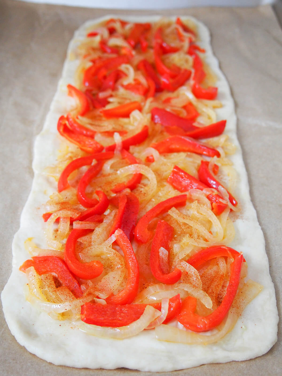 dough for Catalan coca (Spanish pizza) topped with onions and peppers and a sprinkle of paprika before baking.