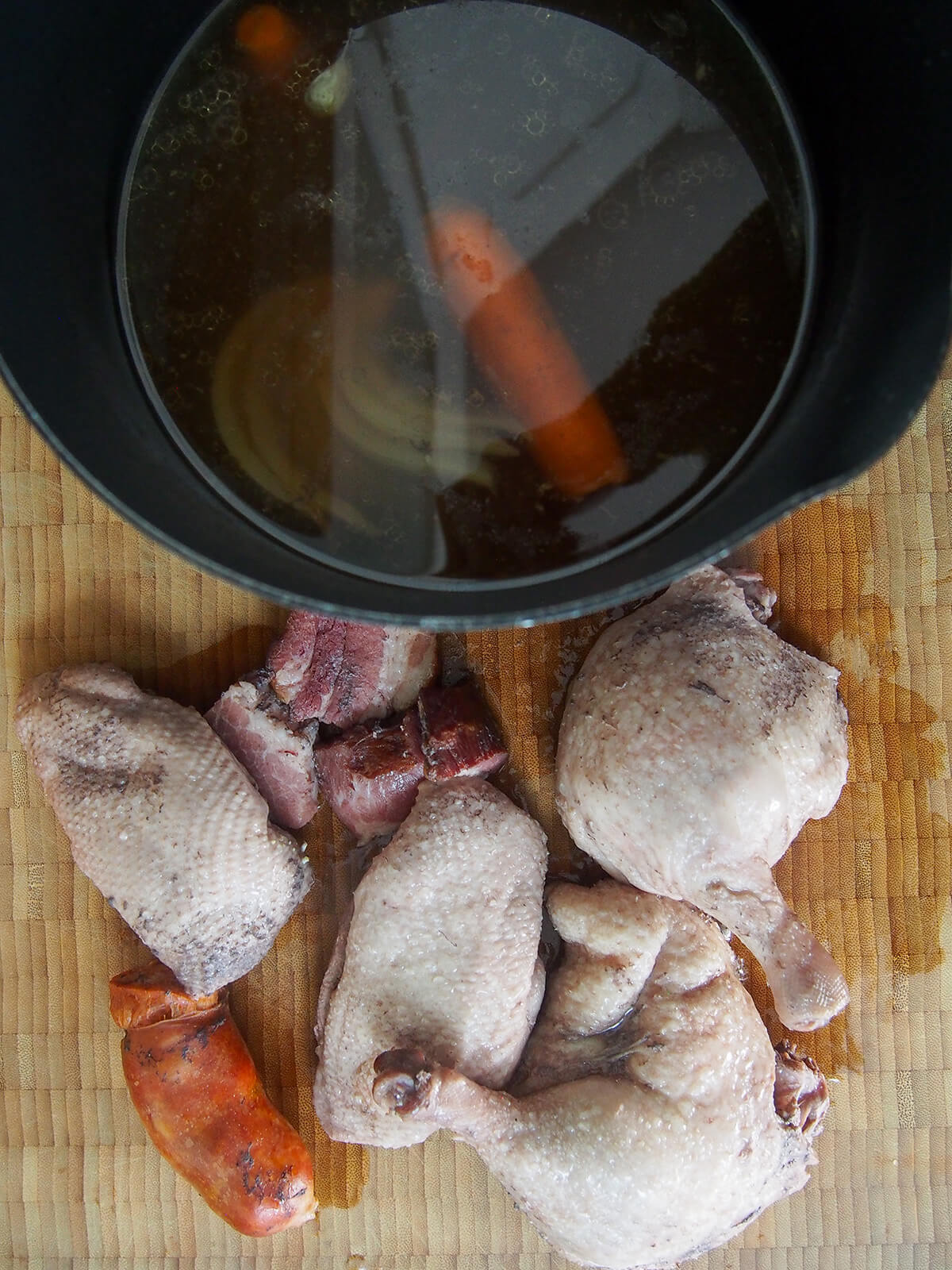 pot with stock and pieces of meat taken out below on board.