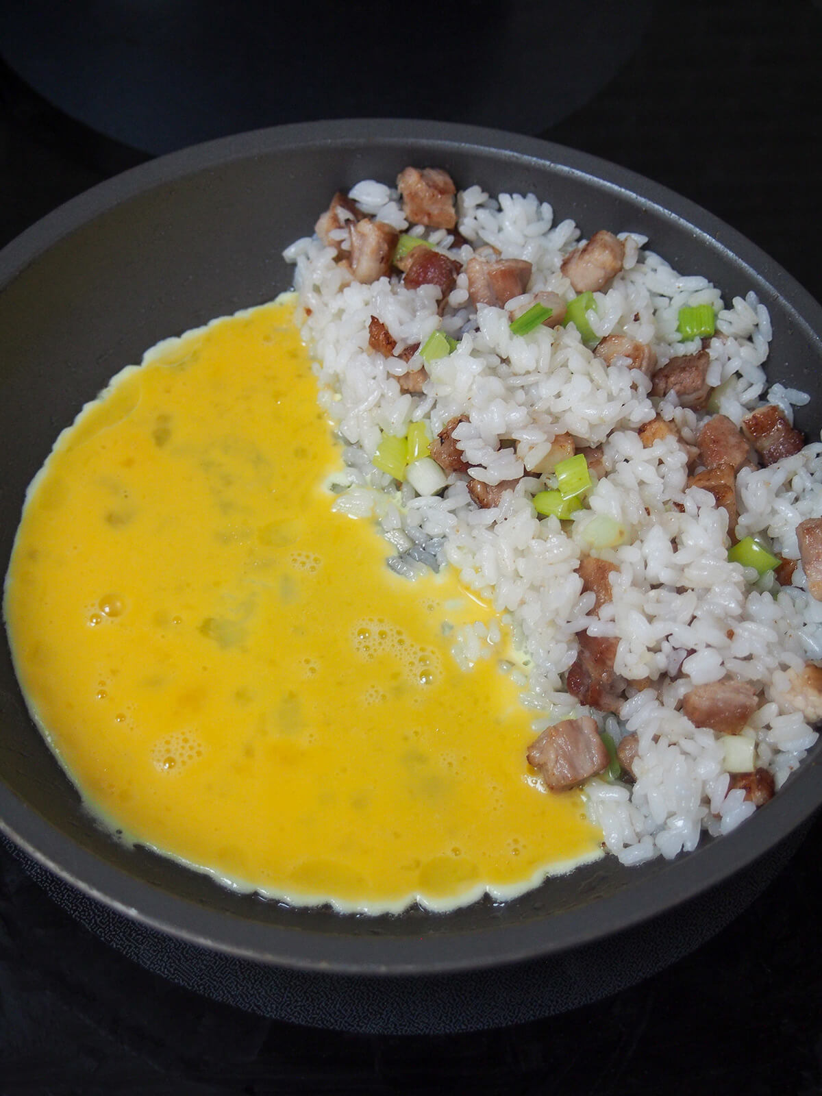 egg scrambling on one side of skillet with rice piled on other side.