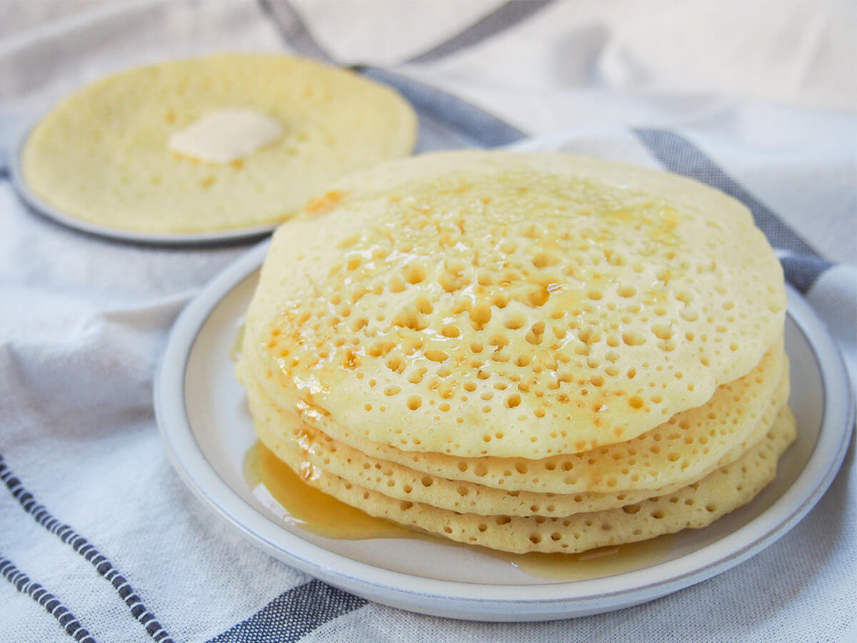 stack of baghrir, Moroccan semolina pancakes baghrir Moroccan pancakes stacked on a plate with honey over them and another in background on plate with butter on top.