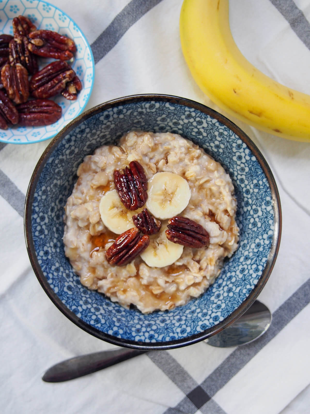 bowl of banana oatmeal form overhead with banana and dish with maple candied cashews above bowl.