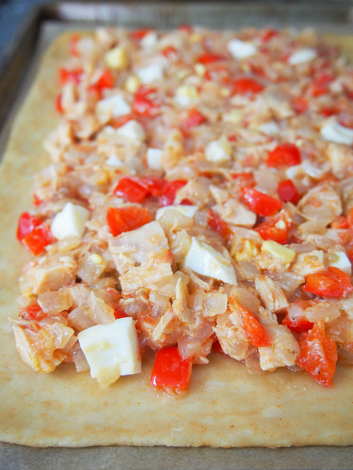 tuna, pepper, onion and egg filling spread over pastry with edge of pastry clear.