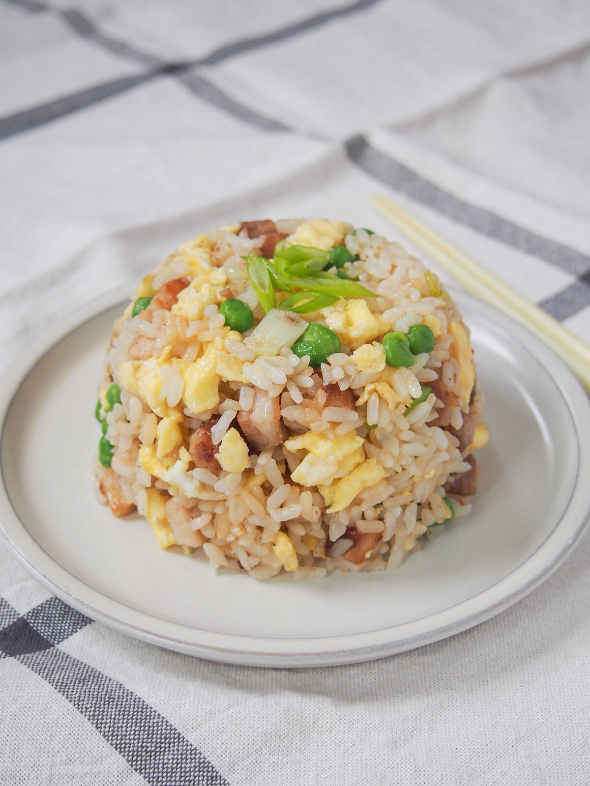 plate of chashu chahan, Japanese fried rice, garnished with green slices of spring onion, with end of chopsticks showing behind plate.