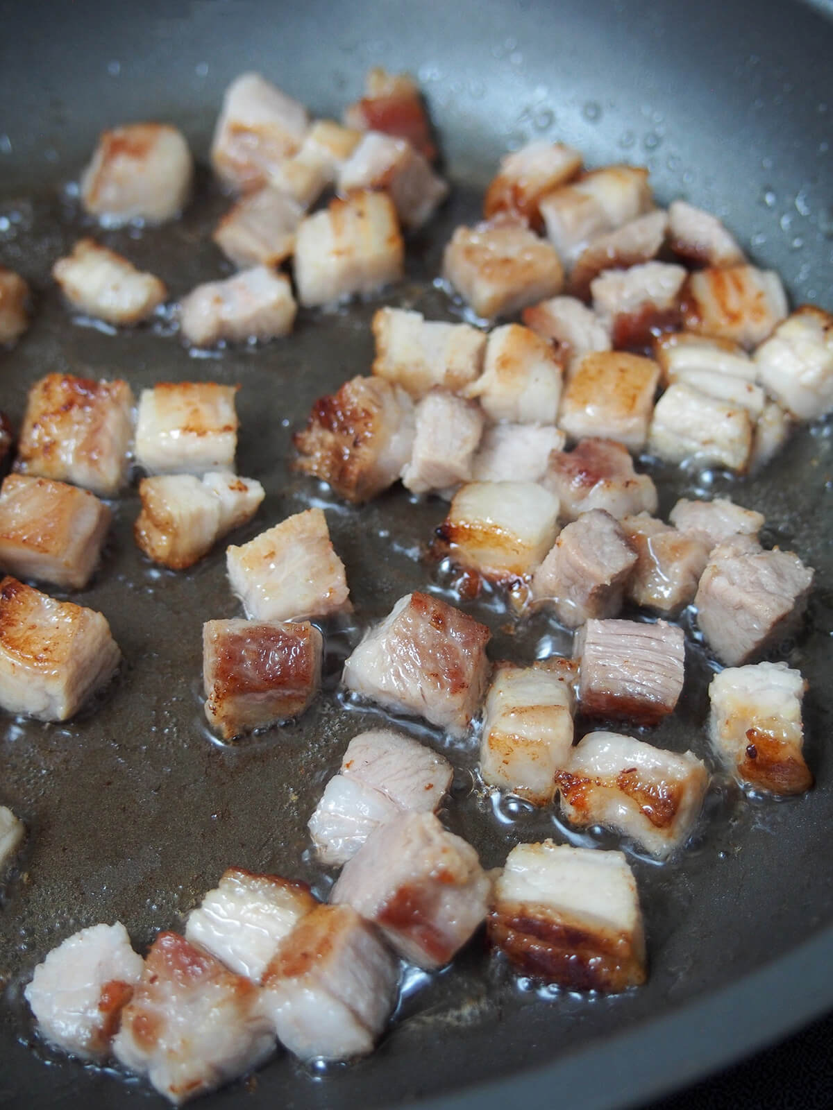 small pieces of pork belly browning in skillet.