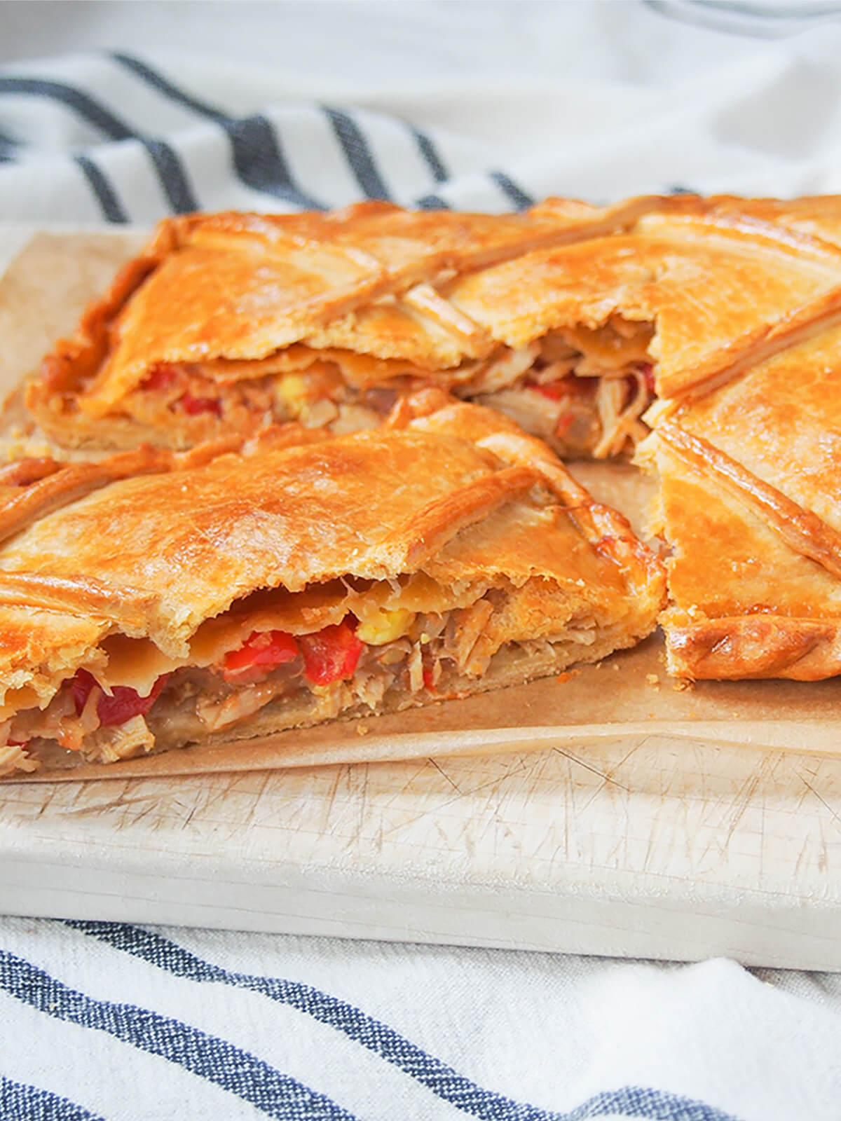 slice of empanada gallega sitting slightly to front of rest of pie on chopping board.