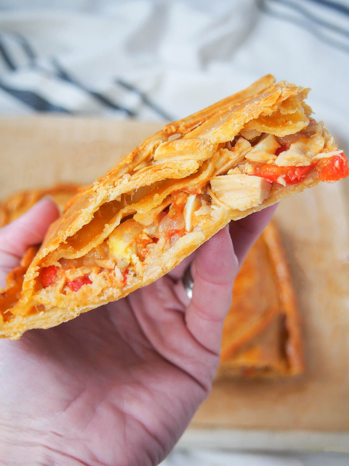 hand holding up a slice of empanada gallega showing tuna and pepper filling.