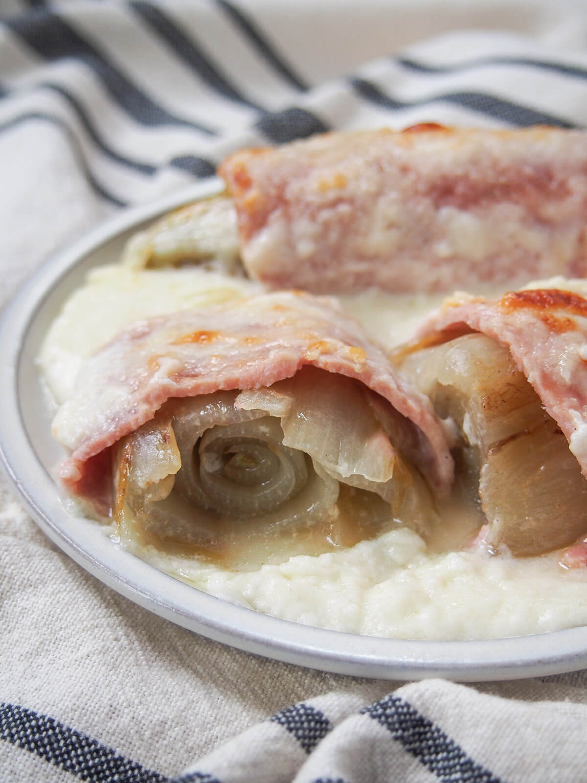 cut endives au jambon showing layers of the Belgian endive, ham and sauce over top and around on plate.