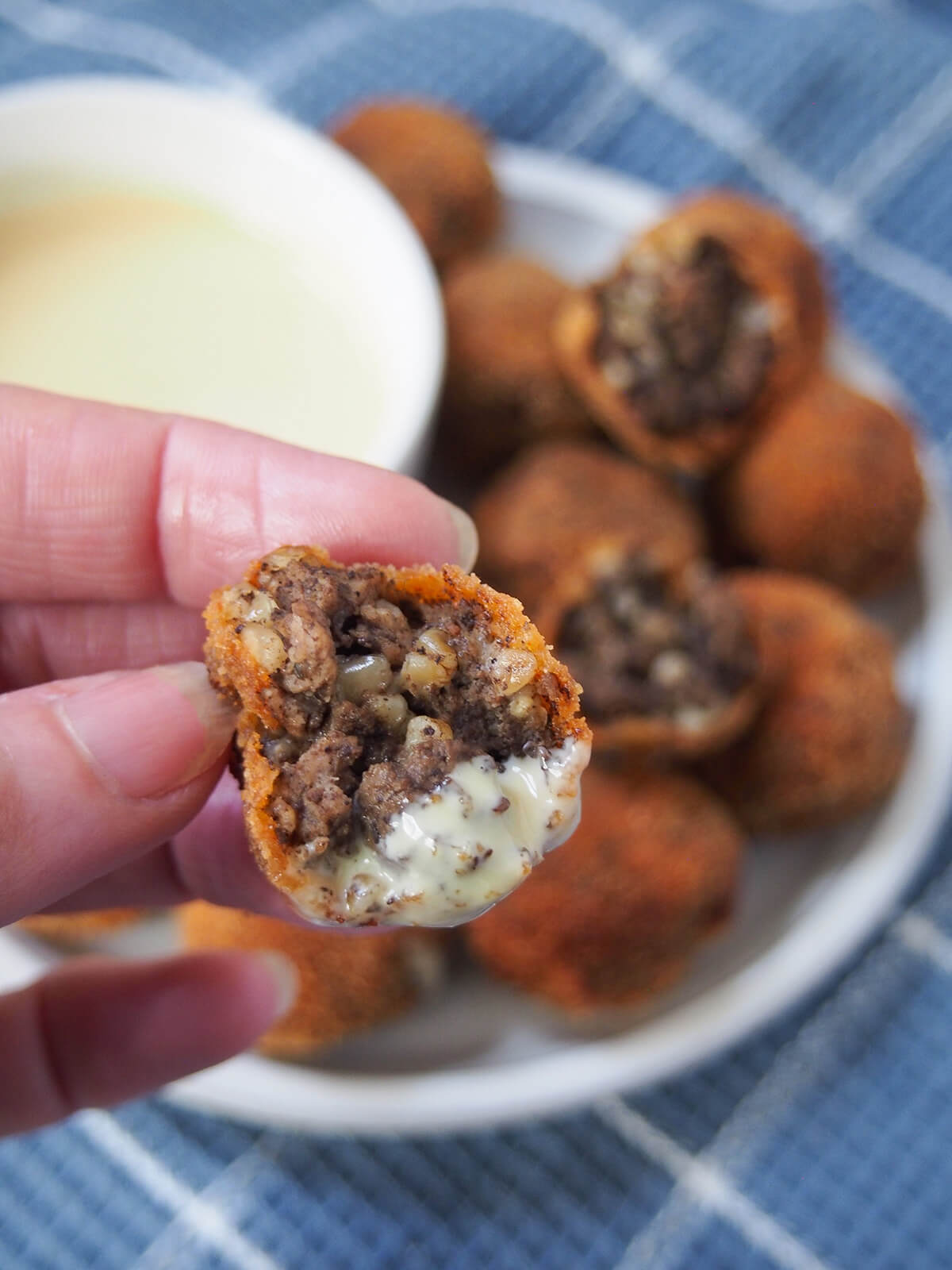 haggis bon bons holding a bitten haggis bon bon in hand over plate with more.