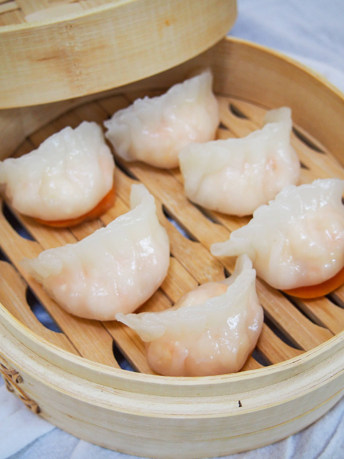 Har gow are a classic and delicious Cantonese dim sum, often called crystal shrimp dumplings due to their slightly translucent wrapper. The filling is simple as it's all about the juicy shrimp. They can be fiddly at first, but you get in the flow and it's well worth the effort. side view of har gow crystal shrimp dumplings in steamer basket.