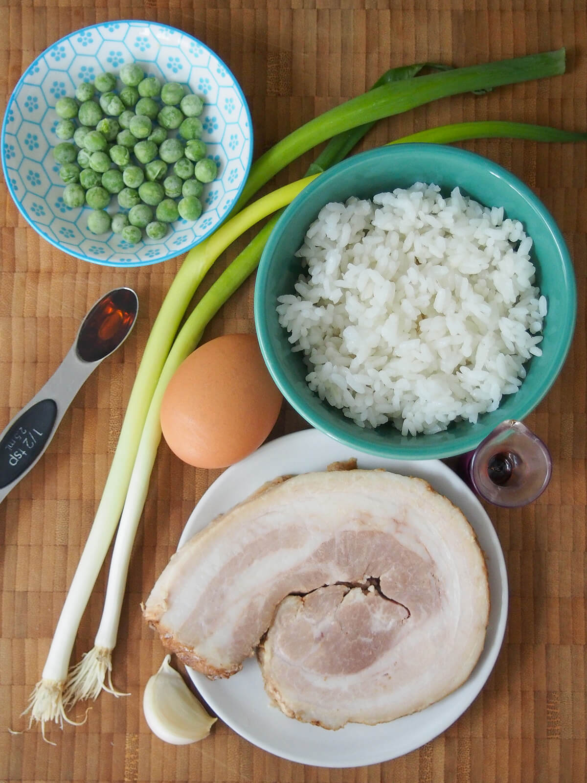 bowl of rice, slice of chashu, egg, spring onions and peas on wooden board.
