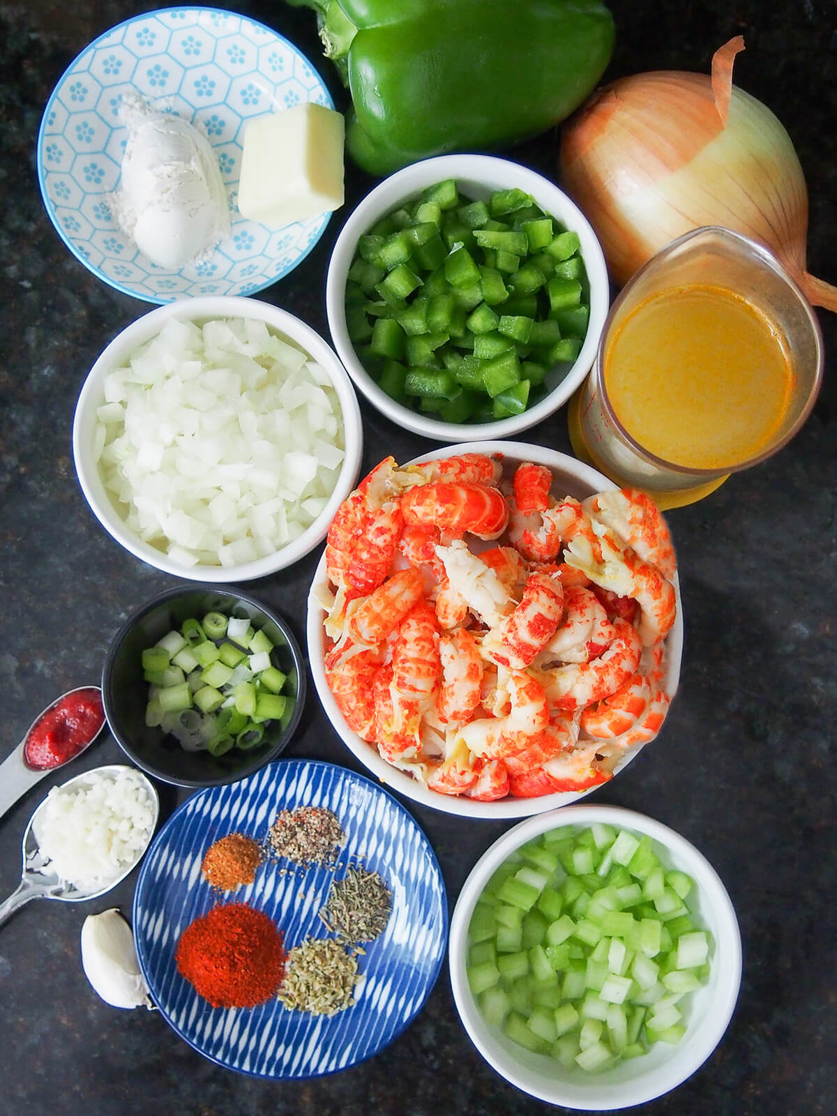 bowls if crawfish, onion, green pepper, celery, plate of spices, measure with stock, dish with butter and flour and some of ingredients around dishes.