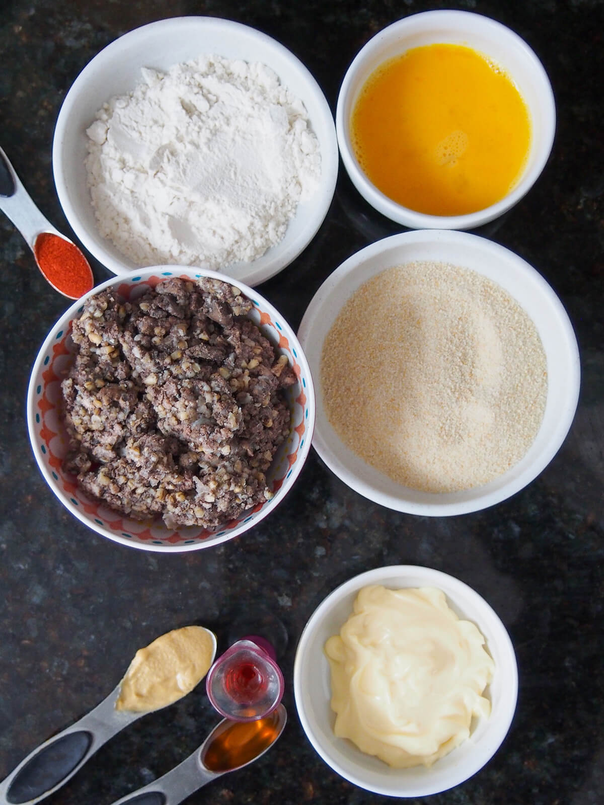ingredients for haggis bon bons overhead view of dishes with haggis, flour, egg, breadcrumbs and mayo below.