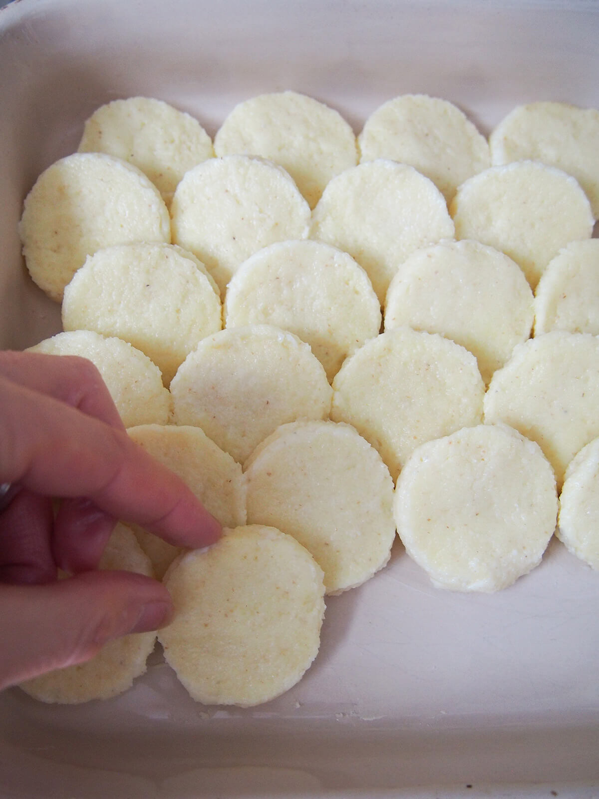 layering circles in top of rows of more circles of the semolina mixture in a baking dish.