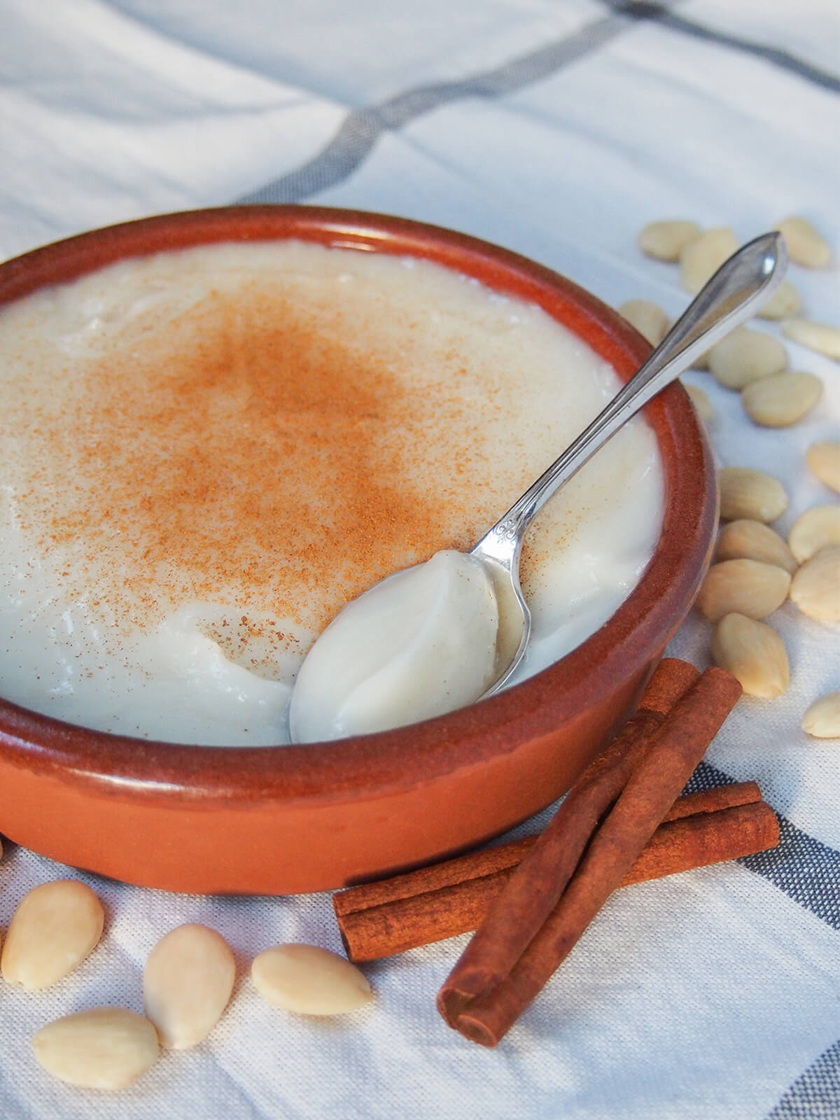 side view of terracotta dish of menjarblanc almond pudding with spoon taking scoop sitting to side.